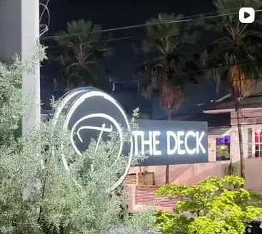 The Deck's illuminated circular D sign and wordmark above Ariapita Avenue at night