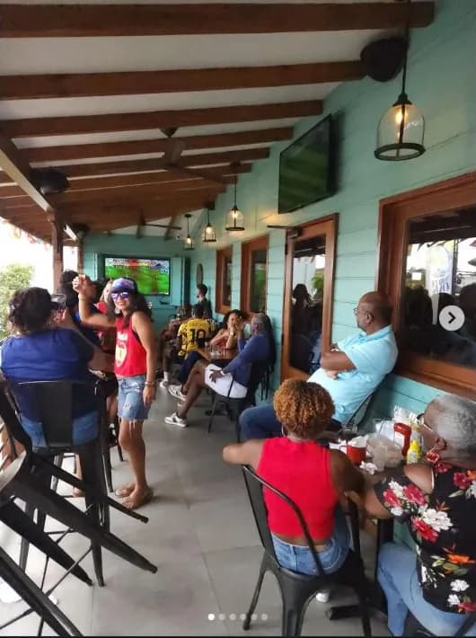 Guests on The Deck's open-air veranda under wooden beams and pendant lights, watching the big screen